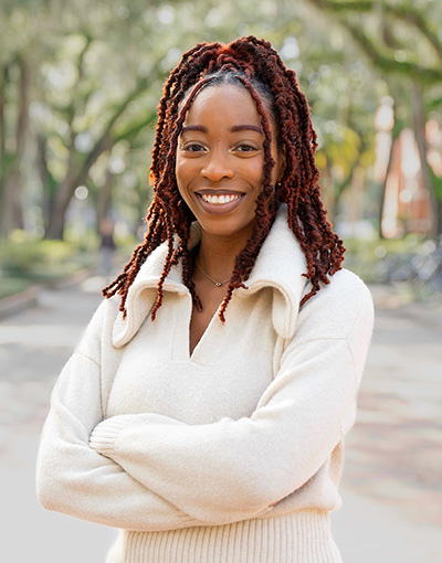 A woman smiling for the camera, outdoors with trees in the background.