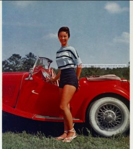 1950s coed posing by a red convertible